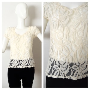 May include: A cream-coloured lace top with short sleeves and a V-neckline. The lace has a floral pattern.
