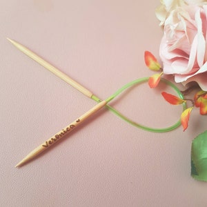 May include: A pair of wooden knitting needles with a green cord. The needles are crossed and the top needle has the name "Veronica" engraved on it.