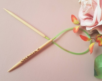 Può includere: Un paio di ferri da maglia in legno con un cordoncino verde. I ferri sono incrociati e il ferro superiore ha il nome "Veronica" inciso su di esso.