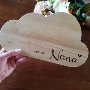 May include: A wooden cutting board shaped like a cloud with the words "Love You Nana" and a heart engraved on it.