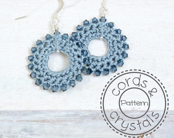 May include: A pair of crocheted earrings with silver hooks and blue crystal beads. The earrings are in the shape of a circle with a hole in the center. The earrings are surrounded by a white background with the text "Cords & Crystals Pattern" in a circle.