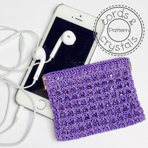 May include: A purple crocheted pouch with iridescent beads, next to a smartphone with white earbuds. The pouch has a rectangular shape with a gold-colored clasp. The image also includes the text "Cords & Crystals Pattern".