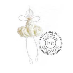 May include: A white crocheted ballerina doll with a crystal bead head and silver wire legs. The doll is hanging from a loop of silver wire. The doll is labeled "Cords & Kit Crystals".