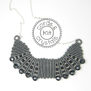 May include: A gray and silver necklace with black beads. The necklace is made of cord and has a fan-shaped design. The necklace is on a white background. The text "Cords & Kit Crystals" is visible in the image.