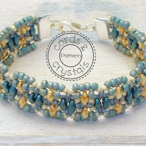 May include: A teal and cream beaded bracelet with a silver clasp. The bracelet is made with small seed beads and has a woven pattern. The bracelet is labelled "Cords & Crystals Pattern".