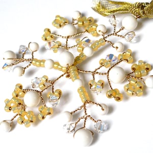 Pode incluir: Um delicado ornamento de arame dourado com contas brancas e amarelas. O ornamento tem a forma de uma árvore com ramos e folhas.