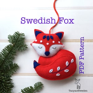 May include: Red felt Swedish fox ornament with white and blue details. The fox is curled up with its tail wrapped around its body. The ornament has a loop for hanging. PDF Pattern.