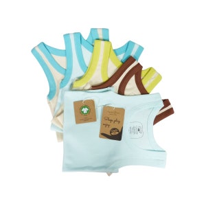 May include: A stack of five sleeveless shirts in various colours, including light blue, white, yellow, and brown. The shirts have a contrasting coloured stripe around the armholes. The shirts are made of a soft, comfortable fabric and are perfect for everyday wear. The shirts have a tag that says "Sleep play enjoy".