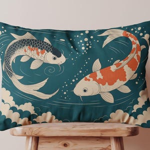 May include: Rectangular decorative pillow featuring a teal background with two koi fish illustrations. One koi is black and orange, the other is orange and white. White bubbles and cloud-like shapes complete the design. The pillow is placed on a wooden stool.
