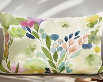 Peut inclure: Coussin rectangulaire décoratif avec un motif floral à l'aquarelle. Le coussin présente un fond crème avec des fleurs colorées dans les tons de rose, de violet, de bleu et de vert. Le coussin est posé sur une surface aux tons neutres.