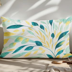 May include: Rectangular decorative pillow with a botanical design. The pillow features a white background with a watercolor pattern of teal, yellow, and light green leaves and stems. The pillow is placed on a neutral-toned surface.