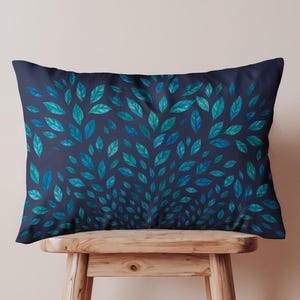 May include: Rectangular cushion featuring a dark navy blue backdrop adorned with a pattern of teal and blue leaves, symmetrically arranged. The cushion is displayed on a wooden stool.