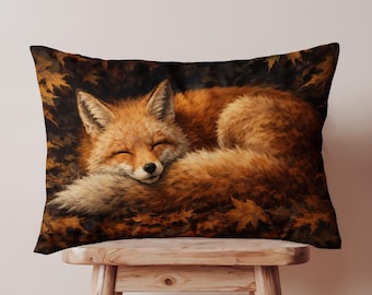 May include: Rectangular cushion featuring a sleeping fox. The fox has orange and white fur and is curled up on a bed of autumn leaves. The cushion has a dark brown background and is resting on a wooden stool.
