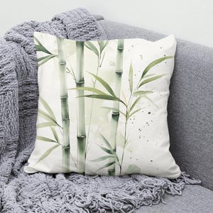May include: A white cushion with a watercolour design of green bamboo stalks and leaves on a white background.