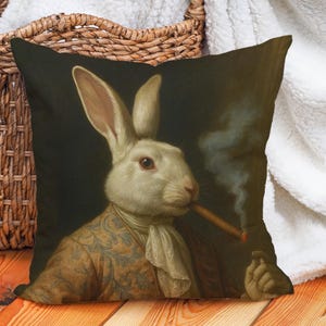 Könnte beinhalten: Dekoratives quadratisches Kissen mit einem Vintage-Porträt eines weißen Kaninchens, das eine Zigarre raucht. Das Kaninchen trägt einen gemusterten Mantel und eine Krawatte vor dunklem Hintergrund.