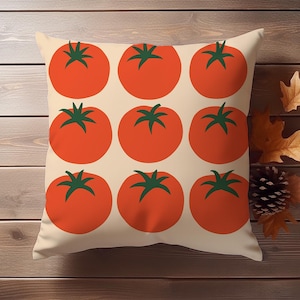 May include: Square decorative pillow featuring a pattern of nine large, stylized red tomatoes with green stems on a cream background. The pillow is displayed on a wooden surface with autumn leaves and a pinecone.
