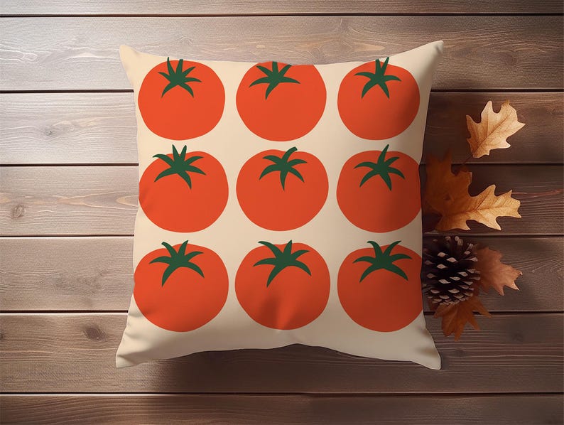 May include: Square decorative pillow featuring a pattern of nine large, stylized red tomatoes with green stems on a cream background. The pillow is displayed on a wooden surface with autumn leaves and a pinecone.