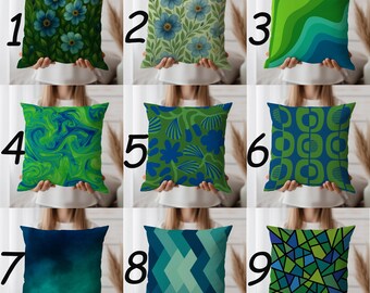 May include: Nine decorative cushions with diverse designs. Cushions feature floral, abstract, and geometric patterns in shades of blue, green, and teal. Each cushion is square-shaped and held by a person.