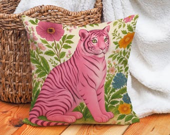 May include: Square decorative pillow featuring a pink tiger with dark pink stripes, set against a floral background with pink, yellow, and blue flowers. The pillow has a cream-colored background and is surrounded by green foliage.