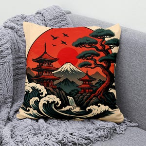 Könnte beinhalten: Quadratisches Kissen mit japanischem Landschaftsdesign. Das Kunstwerk zeigt eine rote Sonne, Pagoden, einen Berg und Meereswellen. Die Farbpalette umfasst Rot, Beige, Grün und Schwarz. Das Kissen liegt auf einer grauen Decke.