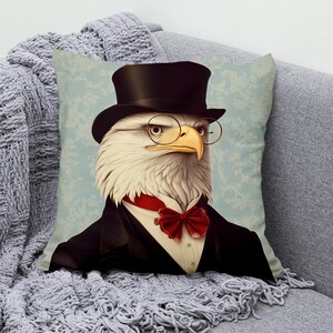 Könnte beinhalten: Dekoratives Zierkissen mit einem vornehmen Adler, der einen schwarzen Zylinder, eine runde Brille und eine rote Fliege trägt. Der Adler ist in einem schwarzen Anzug mit weißem Hemd gekleidet. Der Hintergrund ist ein hellblaues Blumenmuster.