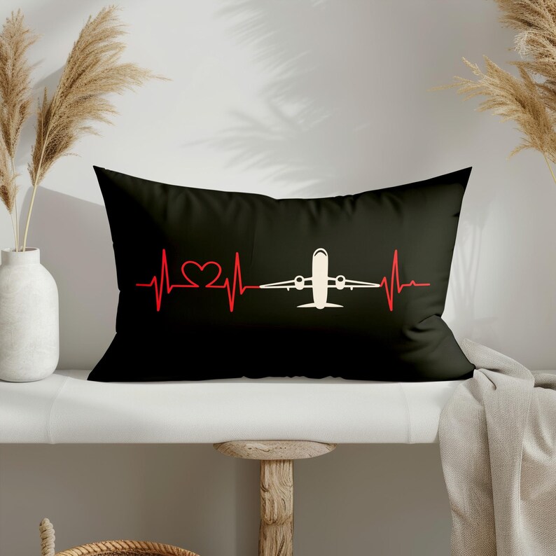 May include: Black rectangular pillow featuring a red heartbeat line design with a heart and a white airplane in the center. The pillow is a decorative item, likely for a bed or couch.