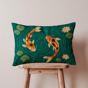 May include: Rectangular decorative pillow with a teal background featuring two orange and black koi fish swimming in a pond with lily pads and lotus flowers. The pillow is resting on a wooden stool.