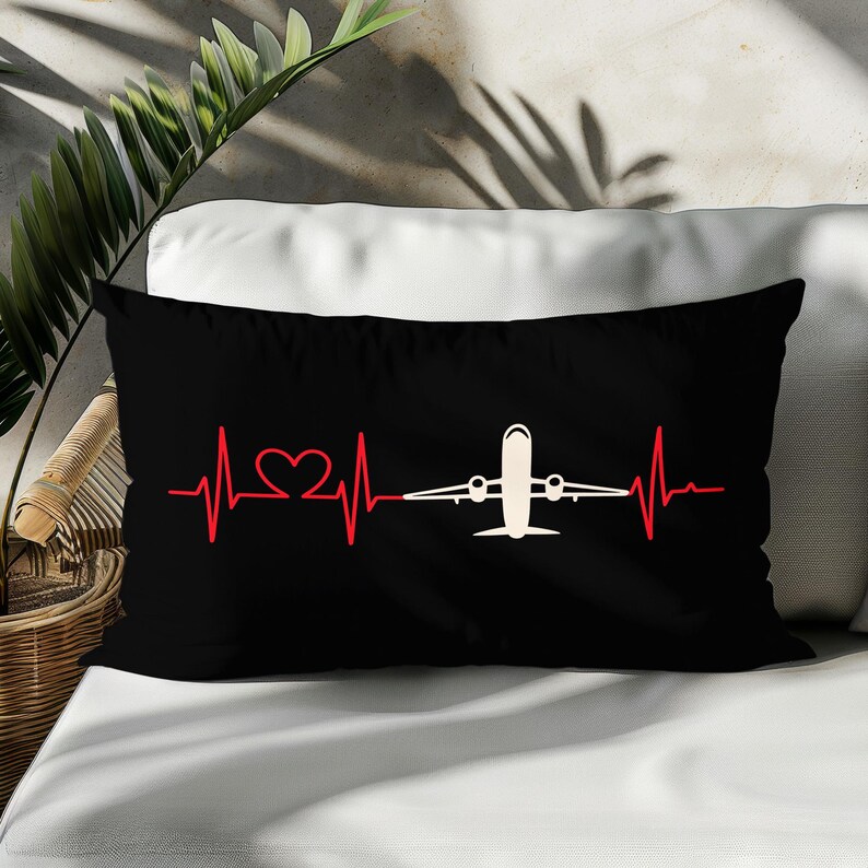 May include: Black rectangular pillow with a red heartbeat line design that includes a heart and a white airplane. The pillow is on a white surface.