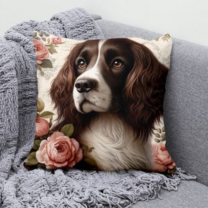 May include: A brown and white Springer Spaniel dog with brown eyes and a pink nose is surrounded by pink roses. The dog is looking to the right of the image. The background is a cream color with a floral pattern.