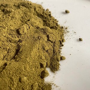 May include: A close-up of a pile of dried, finely ground green powder on a white surface.