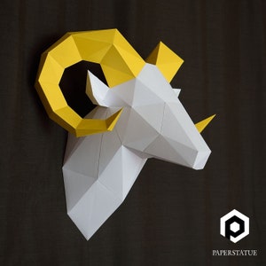 May include: A white papercraft ram's head with yellow horns. The ram's head is made of folded paper and has a geometric design. The horns are curved and point upwards. The ram's head is a decorative piece that can be used to add a touch of whimsy to any room.