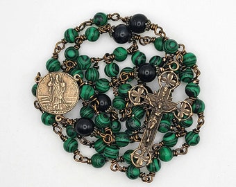 Puede incluir: Un rosario verde y negro con un crucifijo de bronce y una medalla de bronce con un santo. Las cuentas del rosario están hechas de malaquita y ónix.