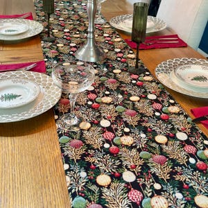 May include: A dining table set with a black floral table runner featuring red, green, and white circular patterns. The table is set with plates, glasses, and cutlery, creating an elegant dining scene. The runner is approximately 180 cm long.