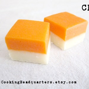 May include: Two square pieces of fudge, one white and one orange, stacked on top of each other. The fudge is on a white surface. The text "CHQ" is in the upper right corner of the image.