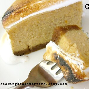 May include: A close-up of a slice of cheesecake with a toasted marshmallow topping. The cheesecake is on a white plate with a fork. The text "CHQ" is visible in the upper right corner of the image.