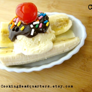 May include: A banana split dessert with vanilla ice cream, chocolate sauce, a cherry on top, and colorful sprinkles. The dessert is served in a white ceramic dish.
