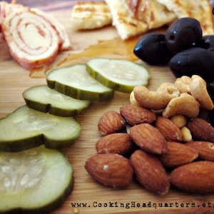 Peut inclure: Un plateau en bois avec une variété d'en-cas, dont des cornichons, des amandes, des noix de cajou, des olives et du jambon roulé. Le plateau est étiqueté "CHQ" et "www.CookingHeadquarters.etsy.com".