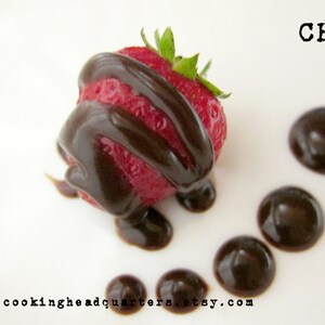 May include: A single strawberry dipped in dark chocolate, with additional chocolate sauce drizzled on a white plate. The text "CHQ" is printed in black on the top right corner of the plate. The text "www.cookingheadquarters.etsy.com" is printed in black at the bottom of the plate.