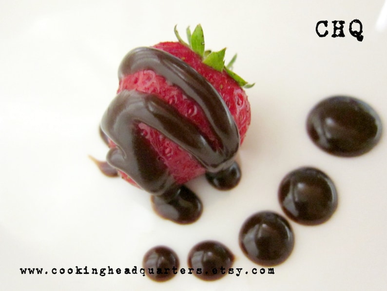 May include: A single strawberry dipped in dark chocolate, with additional chocolate sauce drizzled on a white plate. The text "CHQ" is printed in black on the top right corner of the plate. The text "www.cookingheadquarters.etsy.com" is printed in black at the bottom of the plate.