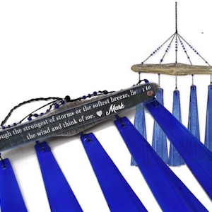 May include: A blue glass wind chime with a wooden top and a decorative inscription. The inscription reads "through the strongest of storms or the softest breeze, listen to the wind and think of me." The wind chime has a heart symbol and the name "Mark".