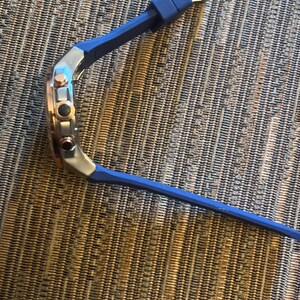 Pu&ograve; includere: Un orologio da polso con cinturino in silicone blu e quadrante argento e oro rosa. L'orologio ha tre pulsanti laterali e una chiusura a fibbia. L'orologio &egrave; appoggiato su una superficie strutturata.