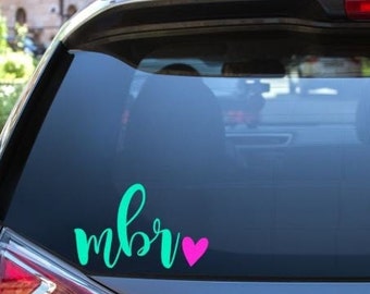 May include: A teal blue car decal with the word "mbr" in cursive lettering and a pink heart.