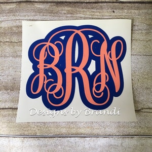 May include: A white vinyl sticker with a navy blue and coral monogram of the letters "BRN". The sticker has the text "Designs by Brandi" below the monogram.