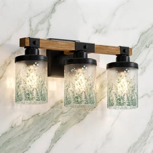 May include: A three-light vanity fixture with a wooden beam and black metal accents. The frosted glass shades feature a green and white botanical design. The fixture is mounted on a marble-patterned wall.