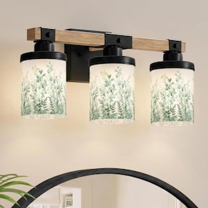 May include: A three-light vanity wall fixture featuring a horizontal wooden beam support with black metal accents. Each light has a cylindrical glass shade decorated with a green botanical fern and eucalyptus leaf pattern, mounted on a black base.