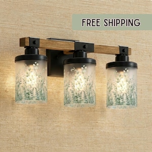 May include: A three-light vanity fixture with a wooden beam and black metal accents. The frosted glass shades feature a green fern design. The fixture is mounted on a textured beige wall.