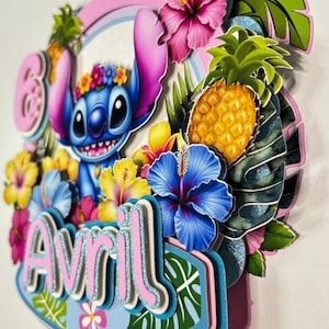 May include: A vibrant cake topper with Stitch, tropical flowers, a pineapple, and the name "Avril". The design incorporates pink, blue, yellow, and green, with glitter details. The overall theme is tropical and celebratory.