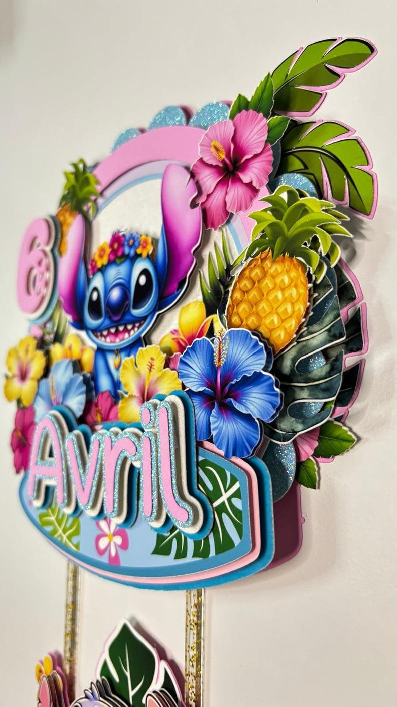 May include: A vibrant cake topper with Stitch, tropical flowers, a pineapple, and the name "Avril". The design incorporates pink, blue, yellow, and green, with glitter details. The overall theme is tropical and celebratory.