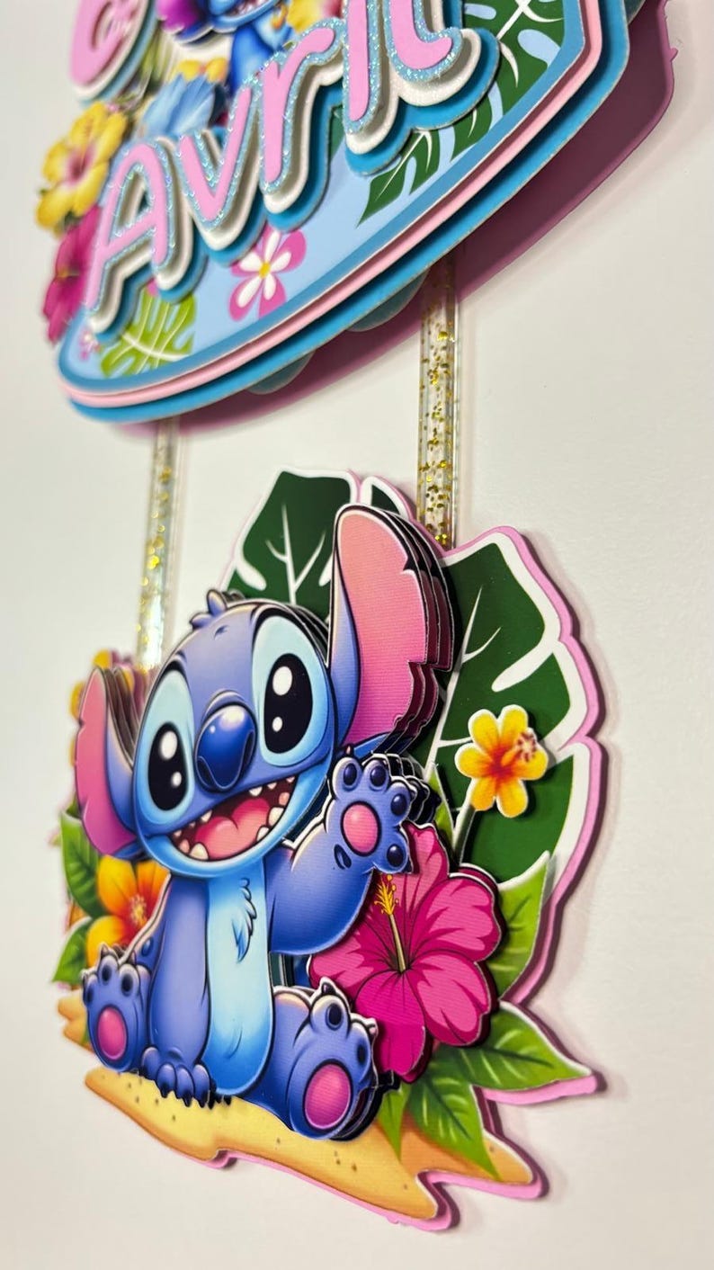 May include: A layered cake topper featuring the character Stitch from Lilo & Stitch. The blue Stitch figure is surrounded by tropical flowers and leaves. The topper also includes the name "Avril" in pink and blue.
