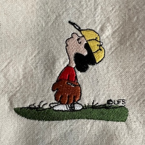May include: Embroidered image of a cartoon character wearing a yellow baseball cap and a red shirt, holding a brown baseball glove. The character is standing on green grass with the word "CUFS" embroidered in white below.